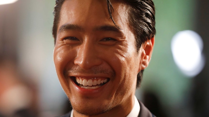 The actor Chris Pang smiling widely, wearing a suit