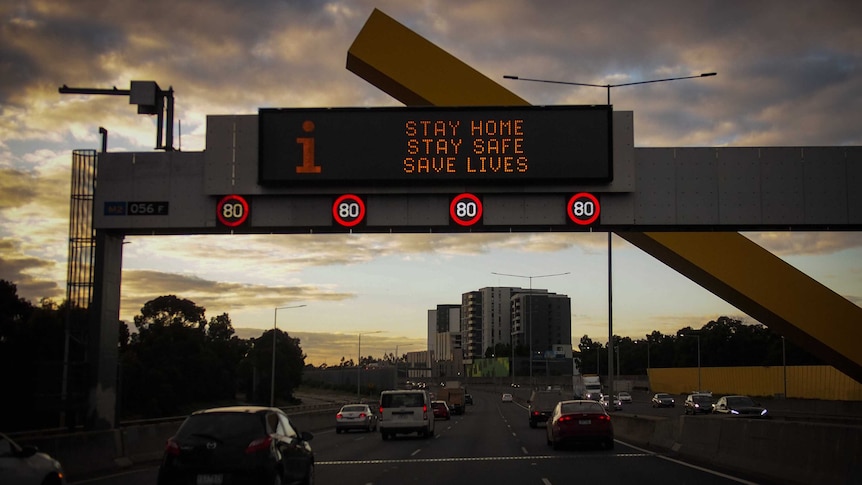 An illuminated sign above a major road that reads "Stay home, stay safe, safe lives".