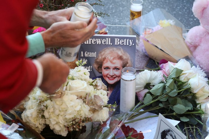 Flowers and candles on a footpath surround a photo of Betty White 