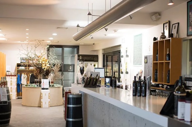 A wine tasting area with bottles of wine stacked on benches and wine barrels.