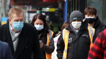 People walking along a Melbourne CBD street wearing masks.