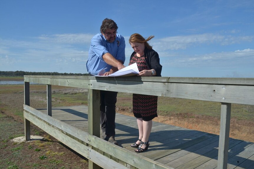 A man and woman stand on a timber boardwalk and study papers