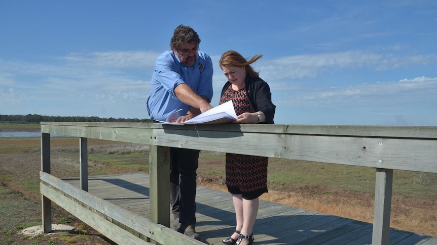 A man and woman stand on a timber boardwalk and study papers