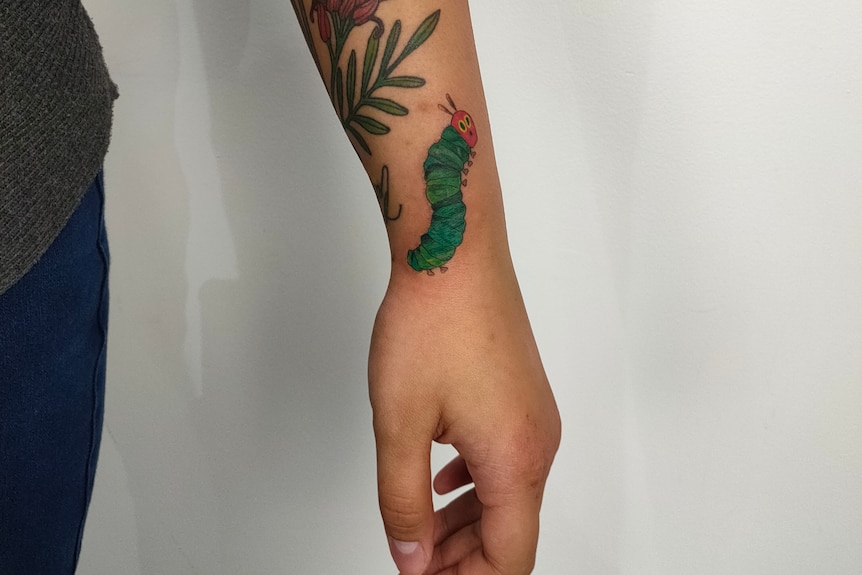 Close-up of a green and red tattoo of the very hungry caterpillar character on a woman's wrist 
