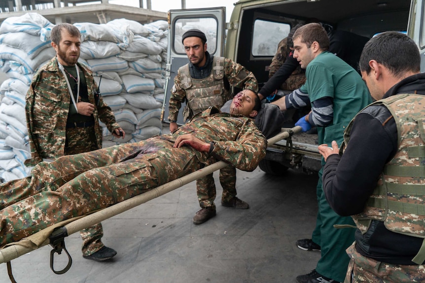 A soldier lies on a stretcher with blood on his face as other men put him in a truck