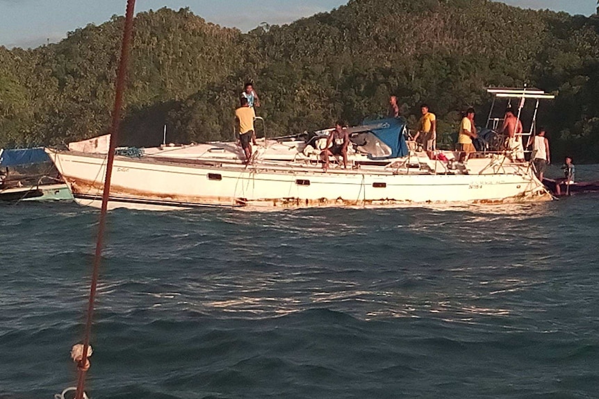 A white yacht, listing, with Philippines sailors aboard.