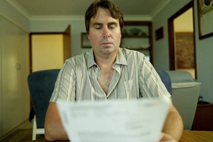 A middle aged man reads from a piece of paper.