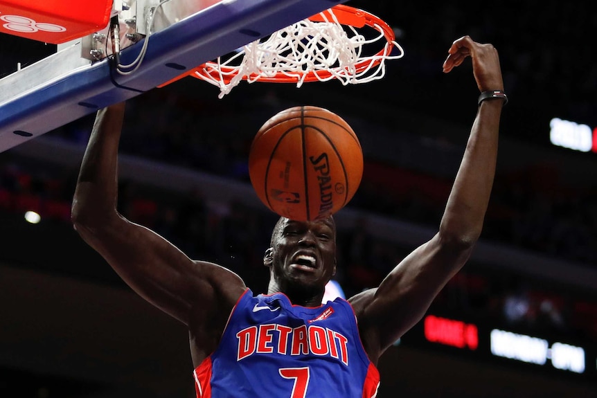 Basketball player slams a basketball into the hoop.