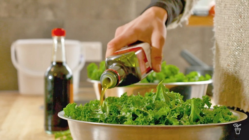 Oil being poured over a shallow bowl of kale.