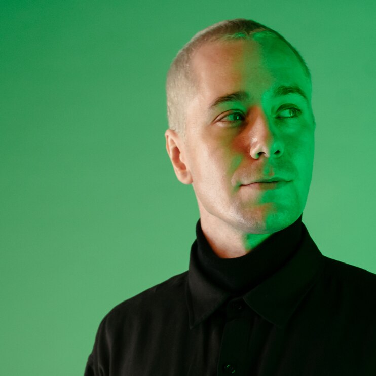 Moss wearing a black turtle neck standing against a green wall