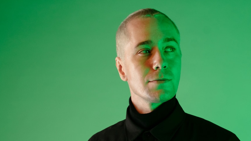 Moss wearing a black turtle neck standing against a green wall