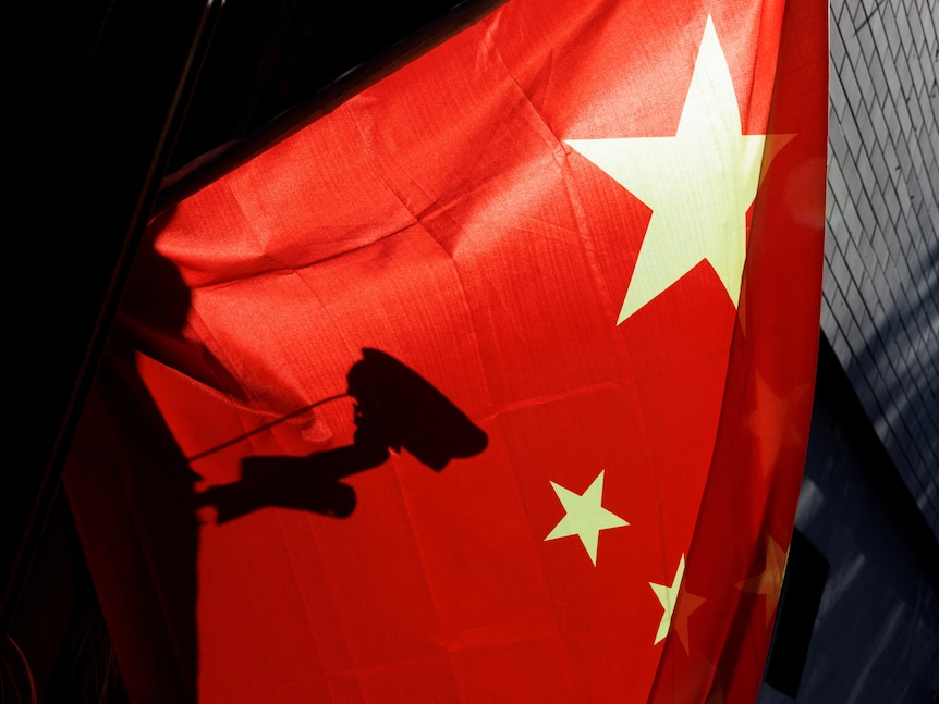 A surveillance camera is silhouetted behind a Chinese national flag in Beijing.