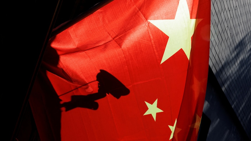 A surveillance camera is silhouetted behind a Chinese national flag in Beijing.