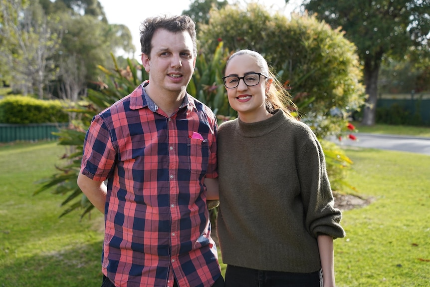 A man and a woman standing close together, outdoors in the sunshine