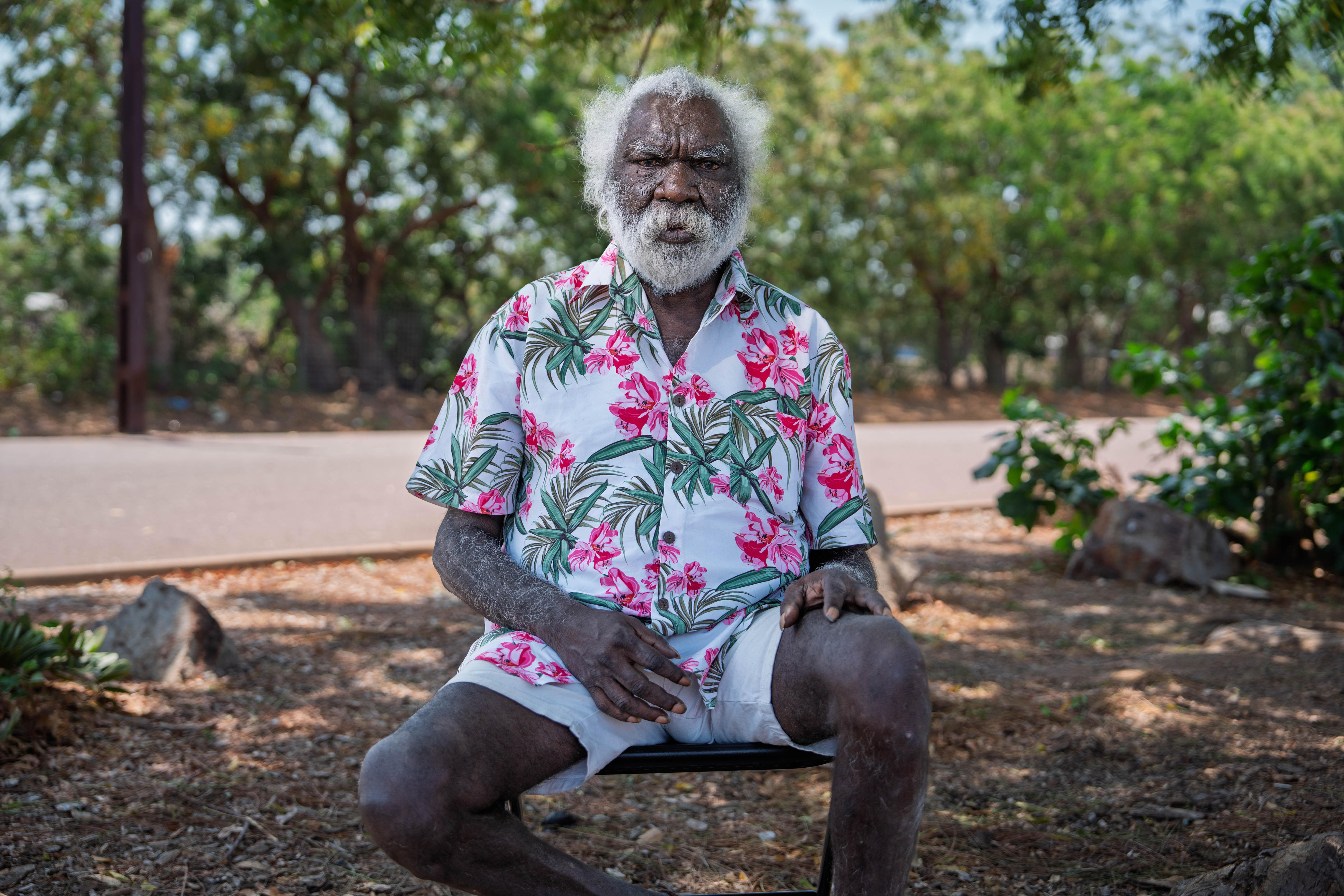 Charlie, an Indigenous man with white hair and a beard, wears a serious facial expression as he looks at the camera.