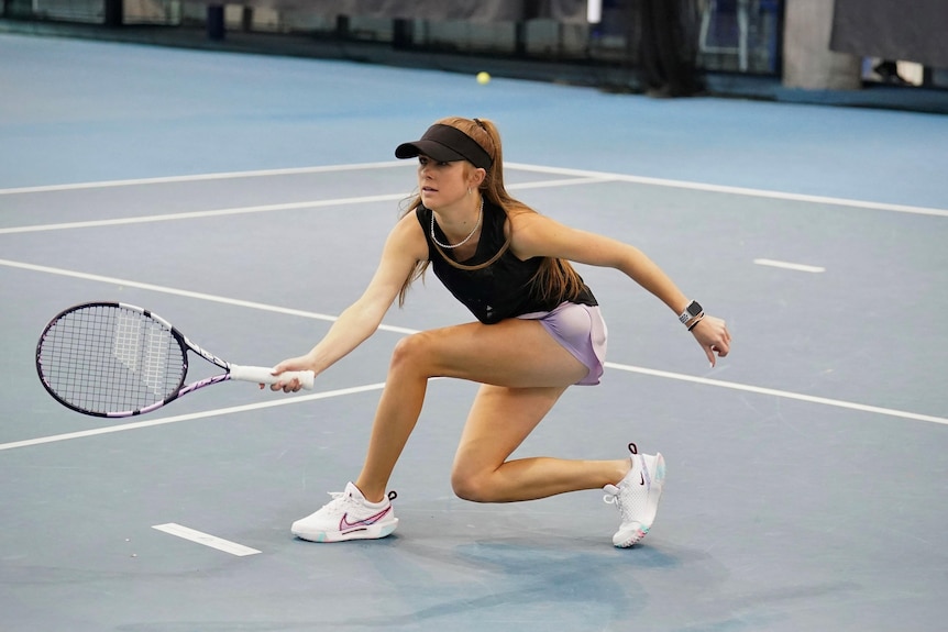 A young female tennis player, wearing a brown visor, lavender shorts,  brown top, plays on a tennis court..