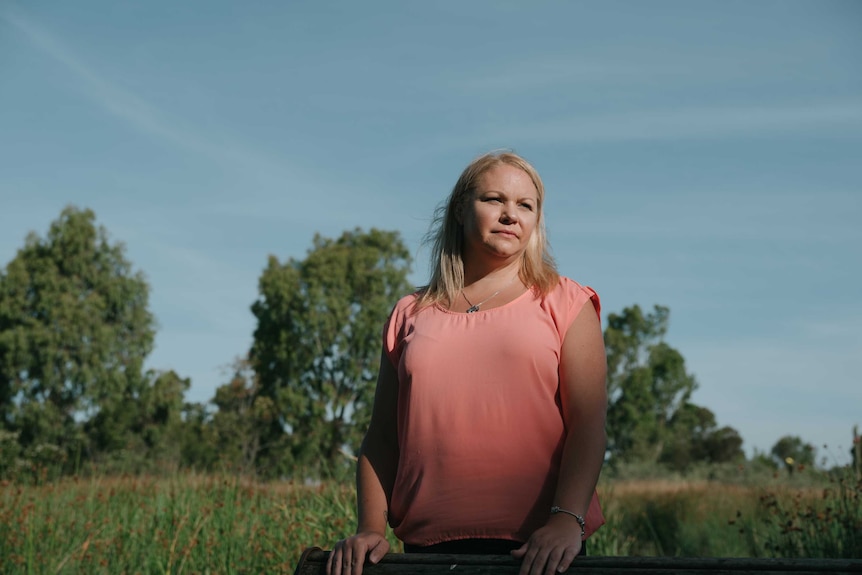 A woman with blonde hair and wearing a pink top looks out to the distance