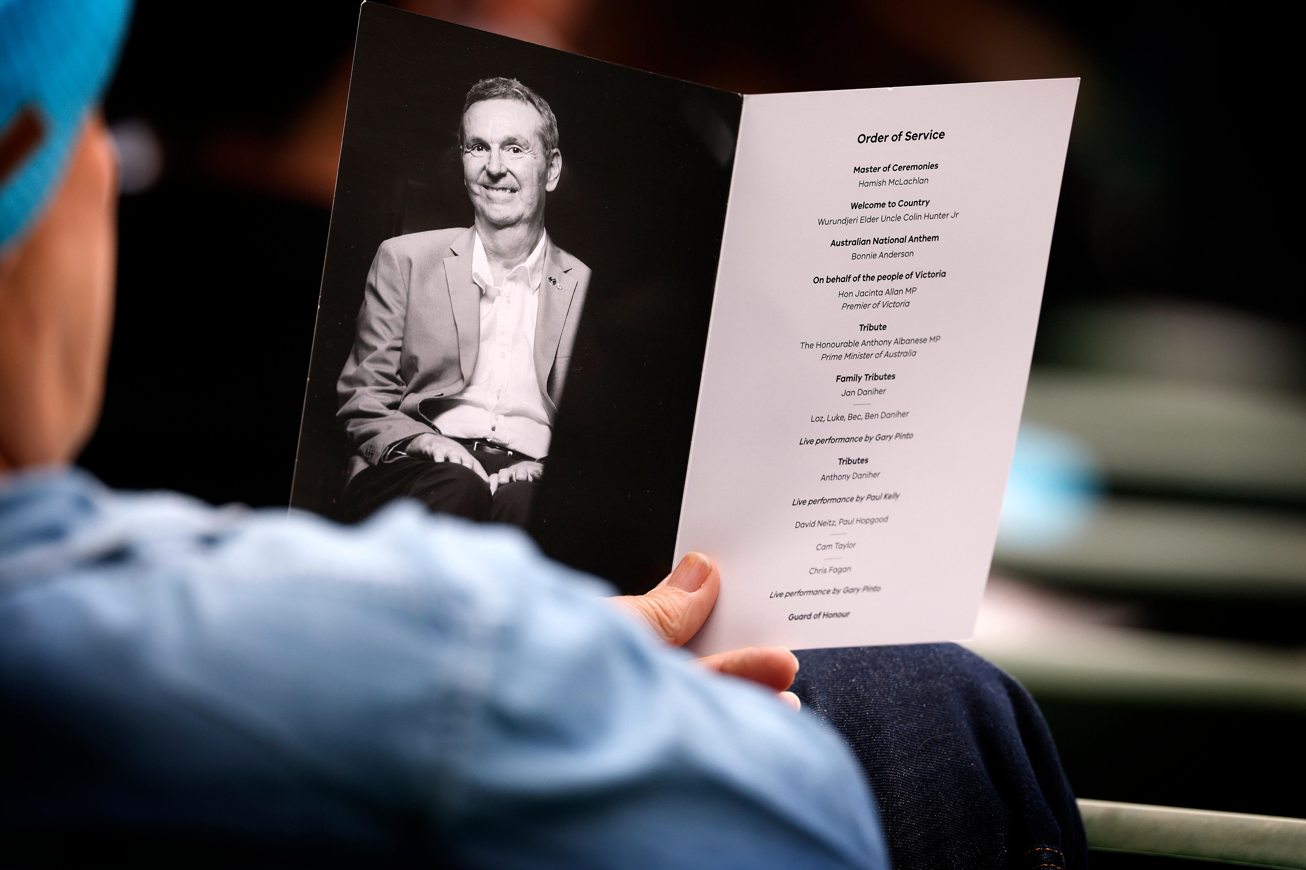 A photo taken over the shoulder of a person in a blue beanie holding a black and white booklet with a picture of a man.