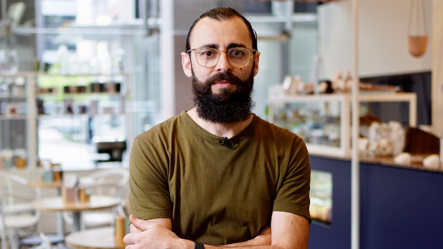 A bearded man with glasses poses for a photo in a coffee shop