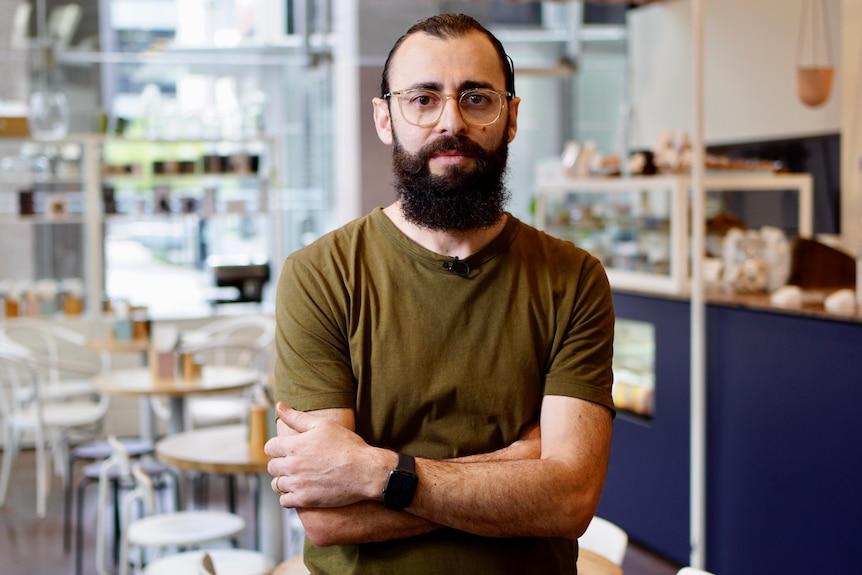 A bearded man with glasses poses for a photo in a coffee shop
