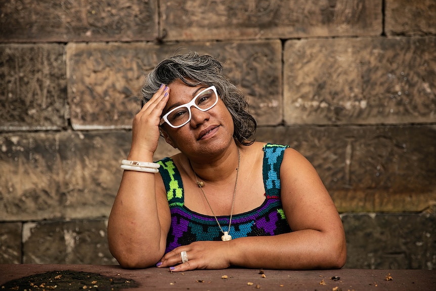 Colour close-up photo of artist Latai Taumoepeau posing in front of sandstone background at the National Art School in Sydney.