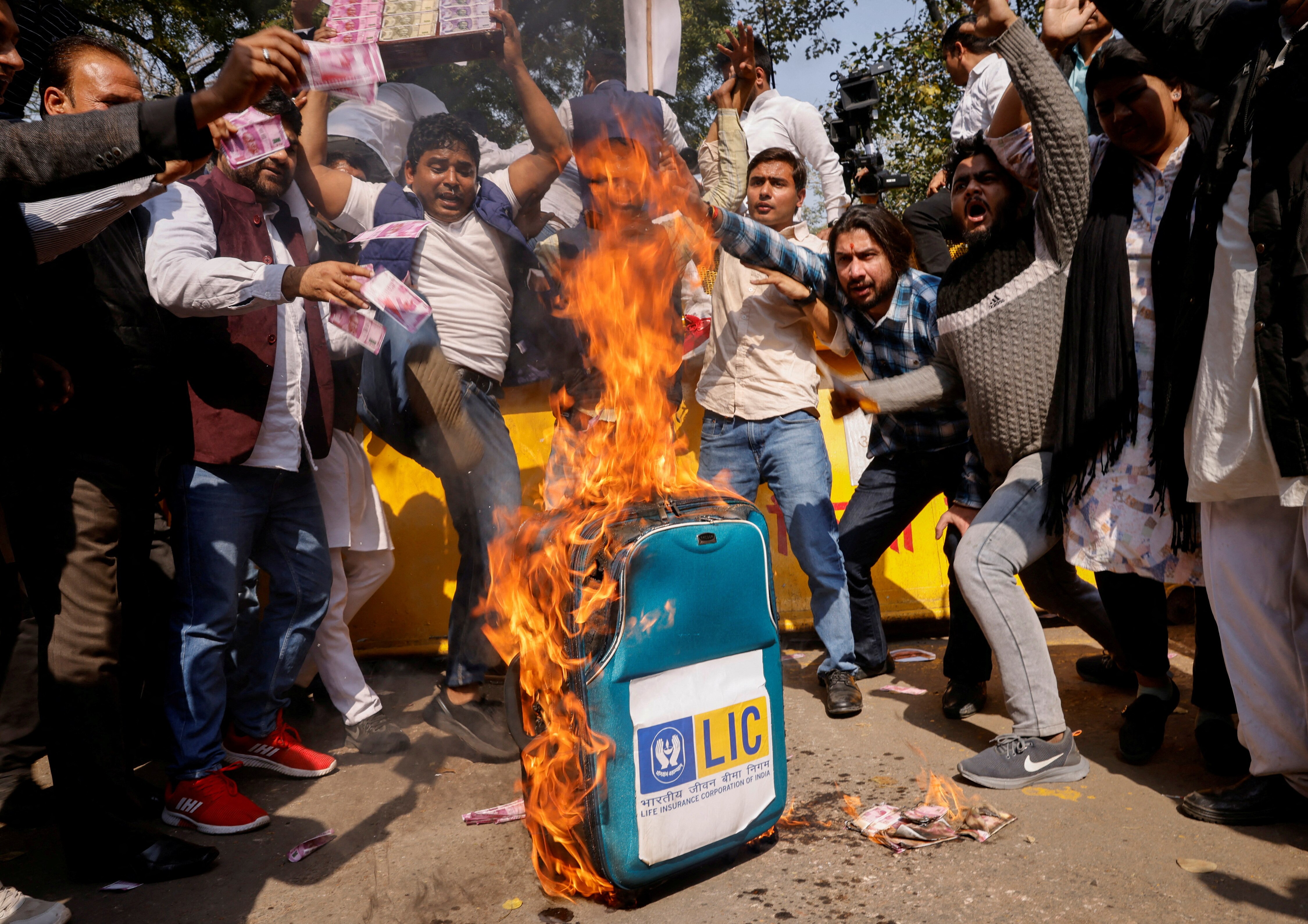 A group of people around a suitcase with LIC written on it, set alight