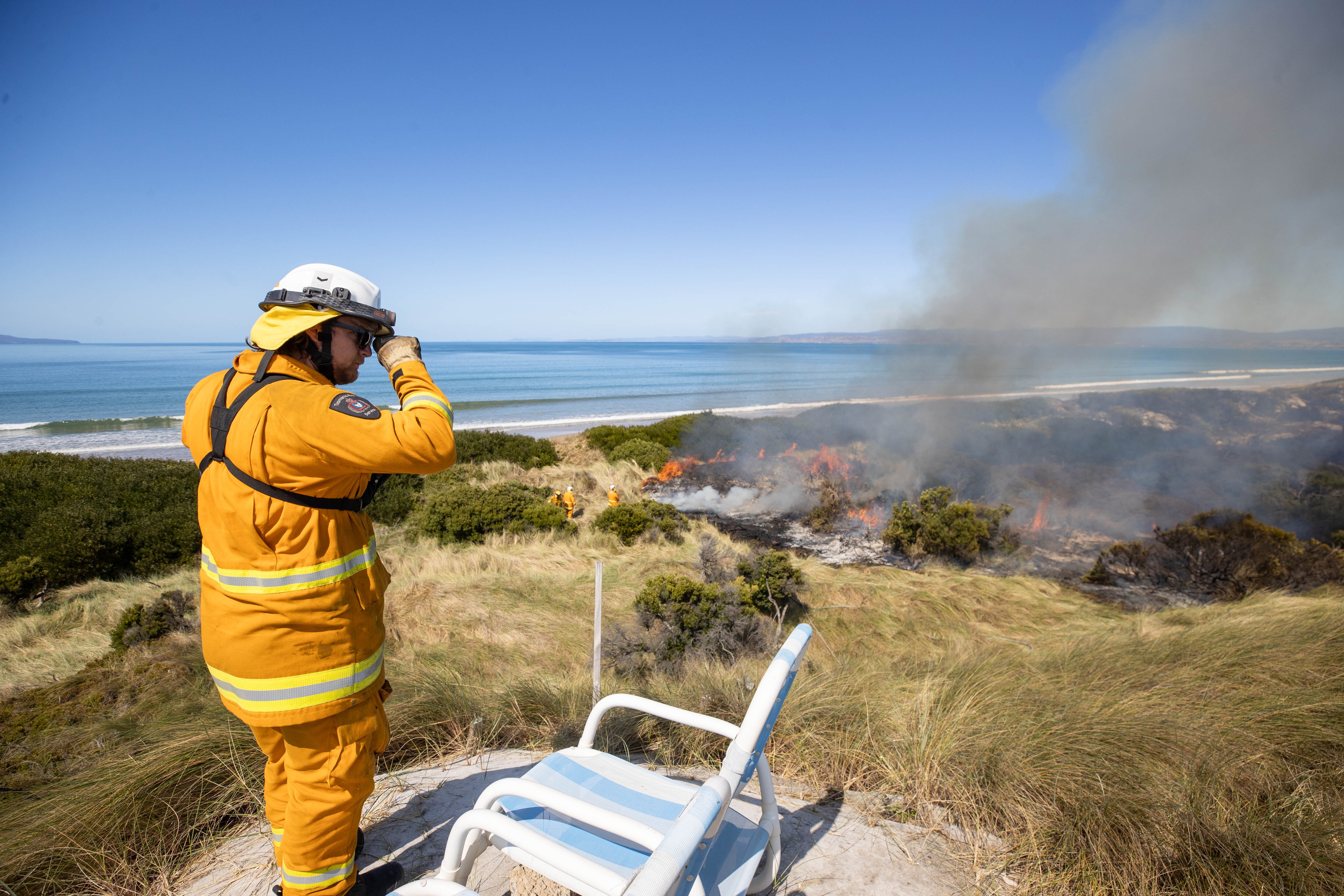 A firefighter looks out from a grassy hill over a fire.