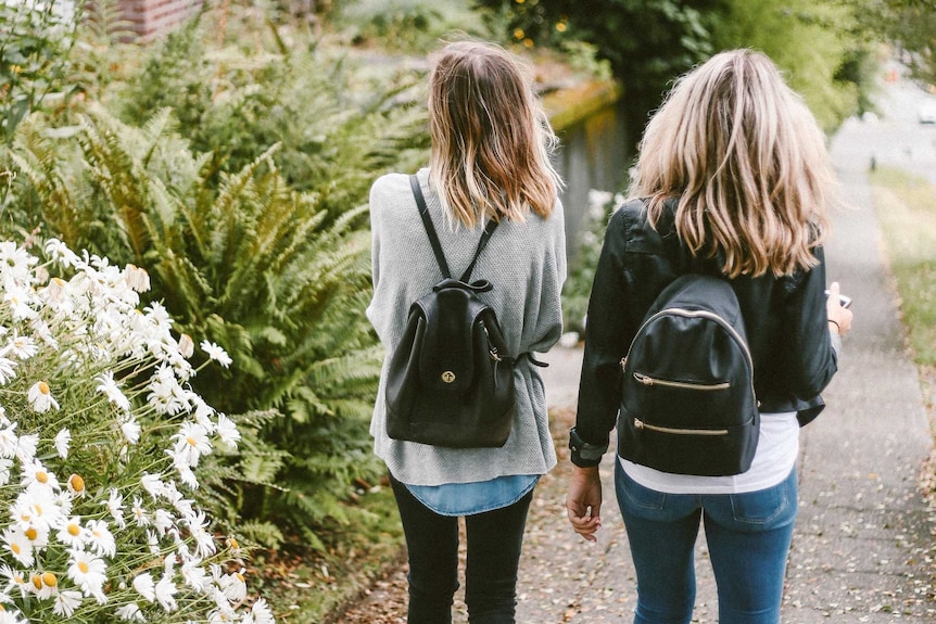 Two teenage girls walk together on a footpath.