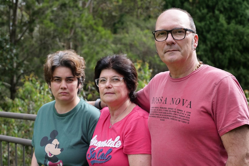 Un homme et deux femmes se tiennent à l'extérieur et regardent la caméra.