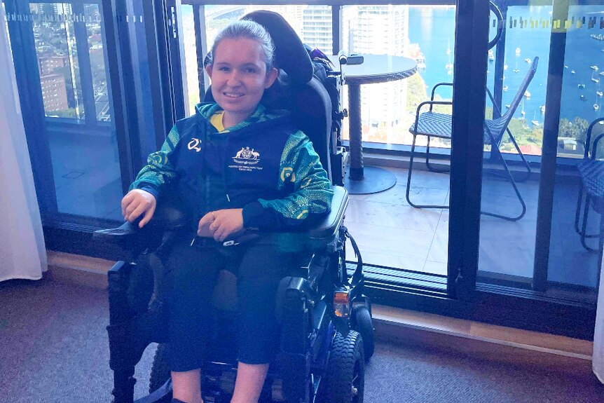 A woman sitting in a modified wheelchair in a high-rise building with buildings in the background