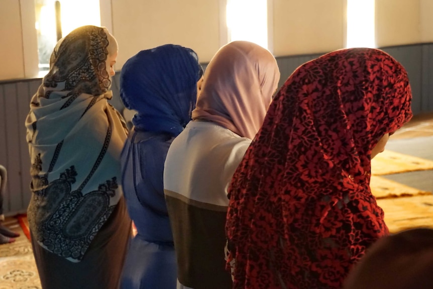 Four woman in headscarfs pray with their backs to the camera.