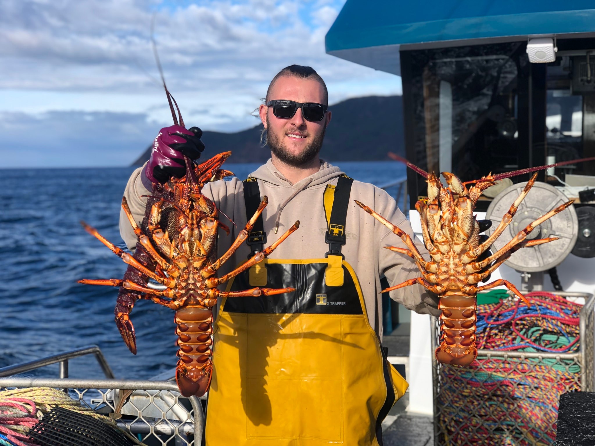 Un hombre sostiene dos langostas en un barco.