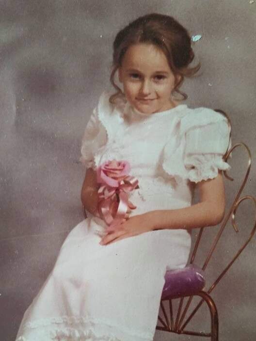 Primary school aged girl dressed as a mini debutante sits on a chair and looks at the camera.