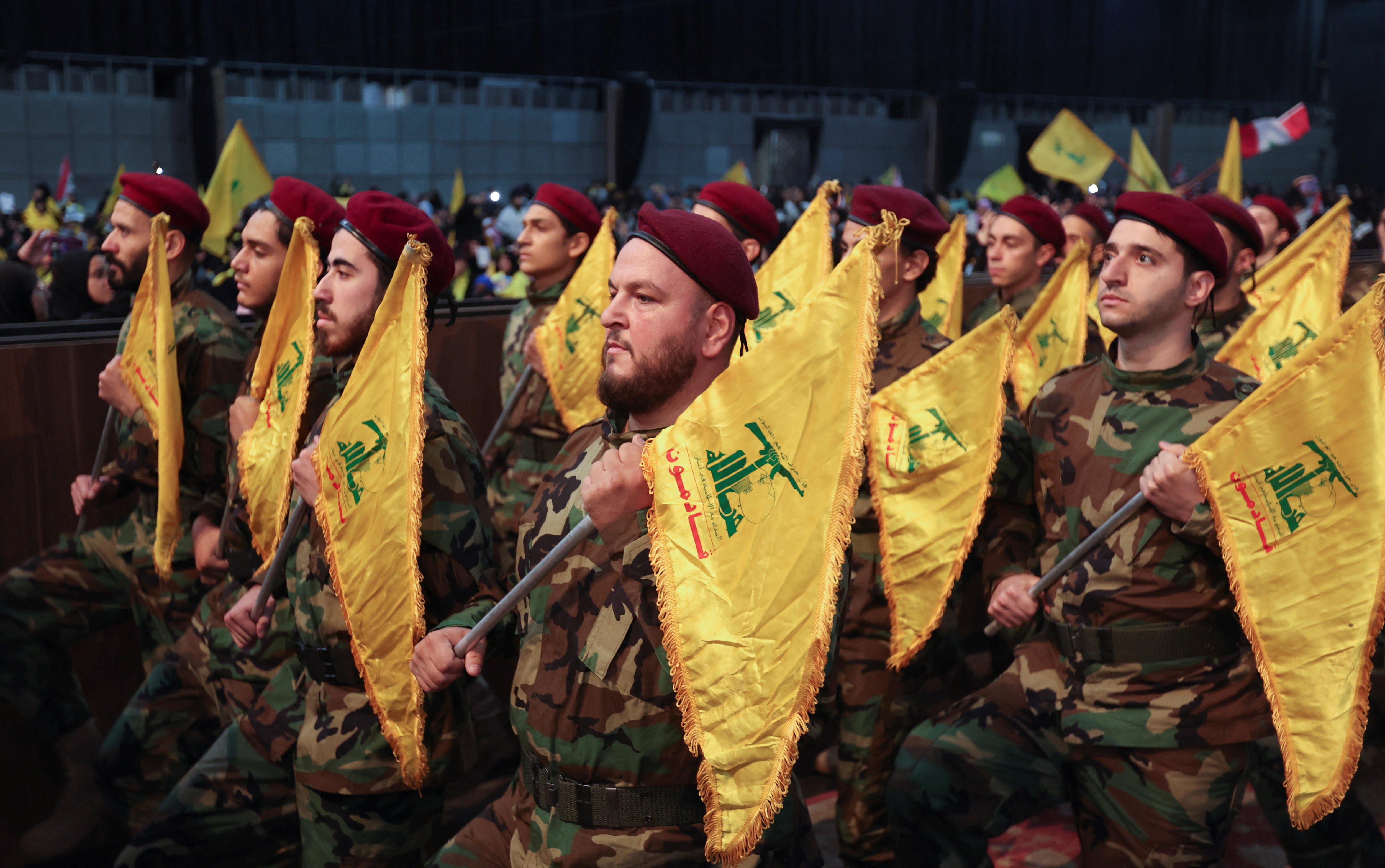 Men in camouflage march with yellow and green flags during a parade 