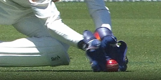 Uma bola toca a grama antes de entrar em um par de luvas de guarda de postigo