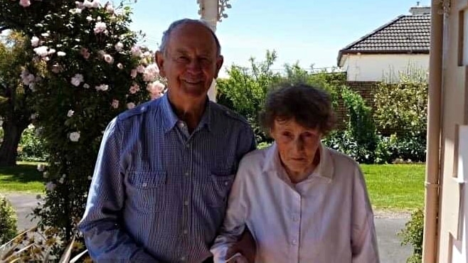 An elderly man and woman standing together on a porch.