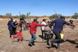 A group of aboriginal people hold hands and dance in a circle