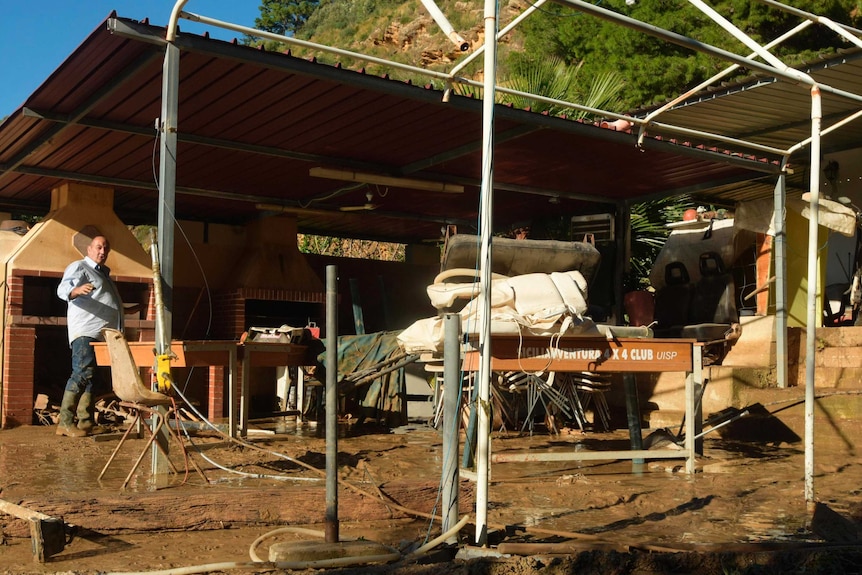 What appears to be the backyard of the flooded house. It is muddy, a man in the backyard is wearing gumboots.