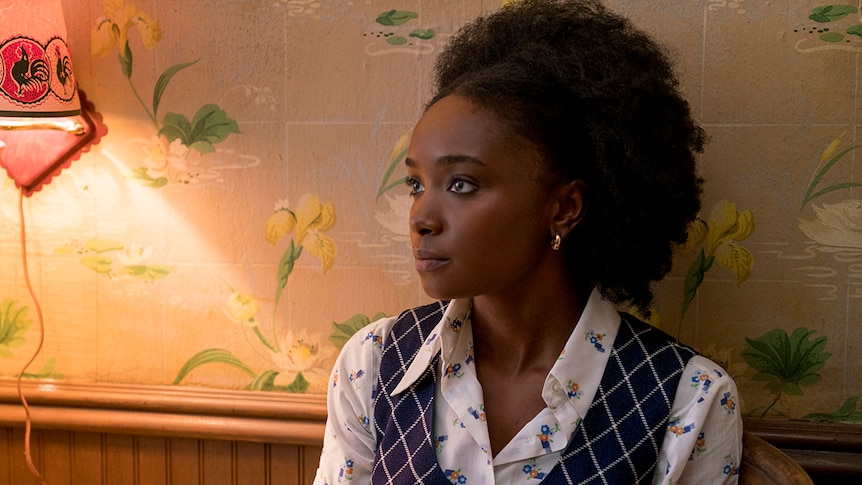 Close-up colour still of KiKi Layne sitting near lamp and against wallpapered wall in 2018 film If Beale Street Could Talk.