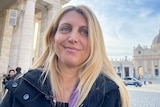 A selfie of a woman with blonde hair outside an ornate building