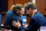 Two white middle aged men in suits huddle in a courtroom