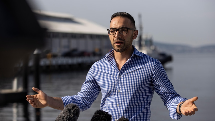 A young man in glasses stands on a waterfront