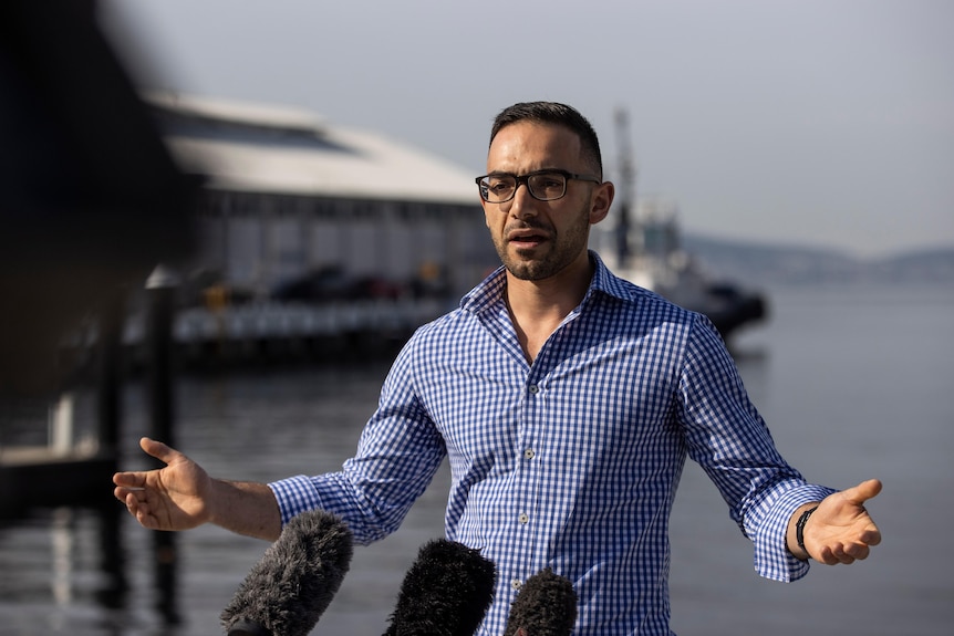 A young man in glasses stands on a waterfront