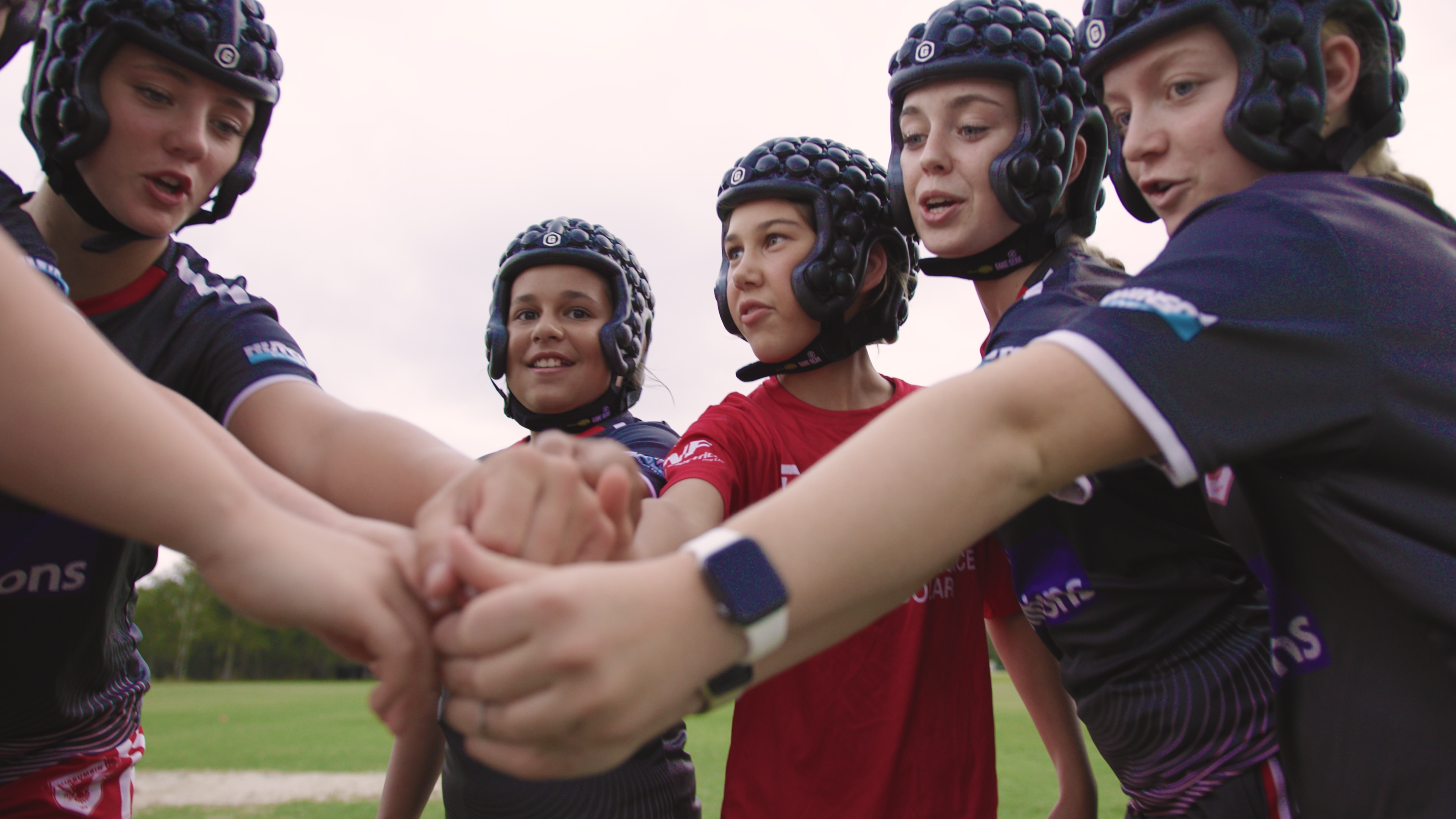 Um grupo de meninas usando capacetes pretos colocou as mãos.