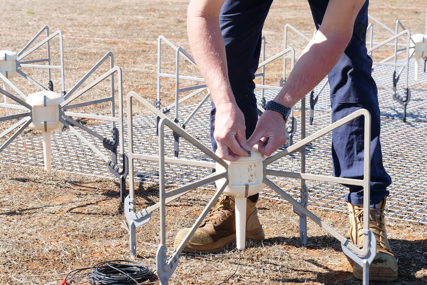A close-up shot of a man's hands handling antennas that are lying on the ground.