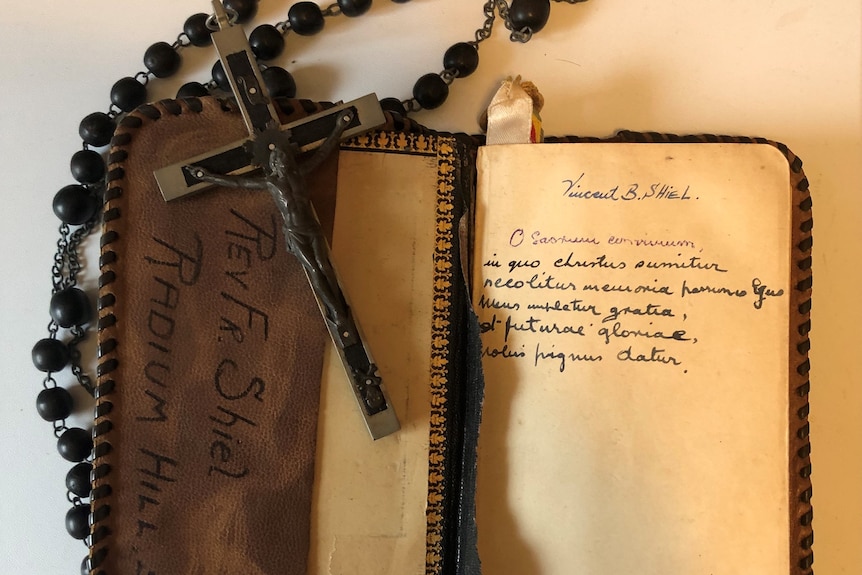 A photo of a rosary and an old bible belonging to Father Shiel with inky handwriting on on page