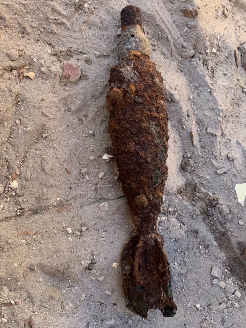An old mortar bomb, sitting in sandy soil.