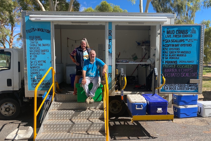 A woman, Lisa, stands with hands on hips behind her brother, Gavin, sitting on an esky inside the doorway of their seafood truck