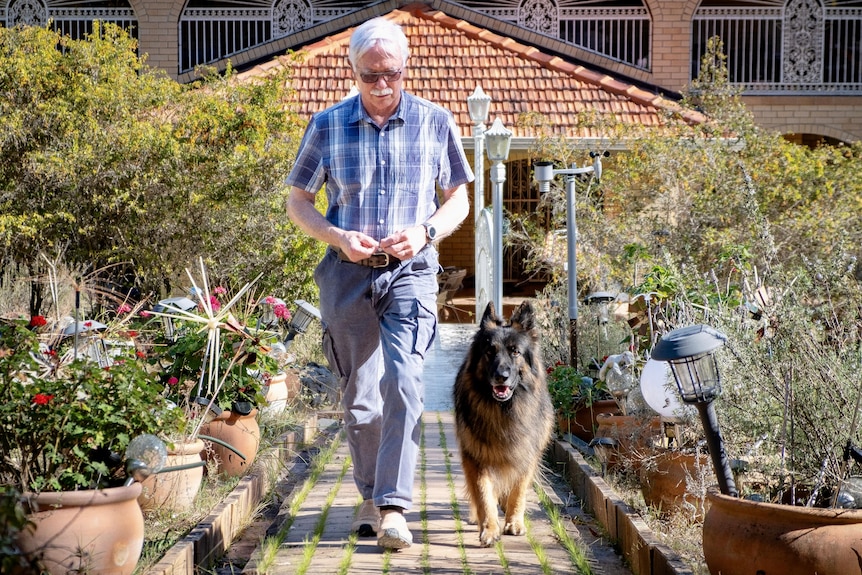 a man walking down a front garden path with a large german shepard 