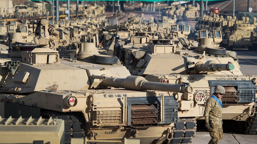A soldier walks past a line of M1 Abrams tanks.